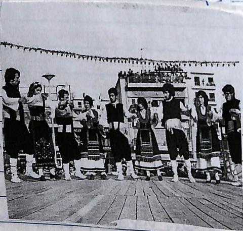 Φωτογραφία εννιά ατόμων (γυναίκες και άντρες) που είναι ντυμένοι με το παραδοσιακό ένδυμα και χορεύουν. Ασπρόμαυρη φωτογραφία