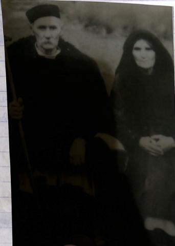 Φωτογραφία ενος ηλικιώμενου άντρα και μιας ηλικιωμένης γυναίκας. Ο άντρας φοράει ενα στραγγάνι(μαυρο στρογγυλό καπέλο), μια κάπα, ενα πουκαμισό ,ενα τσαμαντάνι και τα πουτουρια (είδος παντελονιού). Η γυναίκα φοράει το μπόχο (μαντήλα) ,κατασάρκι , πουκάμισο, την τραχηλιά, ποδιά, φούστα. Ασπρόμαυρη φωτογραφία