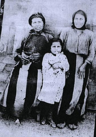 Ασπρόμαυρη φωτογραφία προσφύγων από το 1920. Απεικονίζονται δύο μάνες και ένα μικρό παιδί ντυμένοι με απλά, καθημερινά ρούχα. Οι δύο γυναίκες φορούν μαντήλα στο κεφάλι.